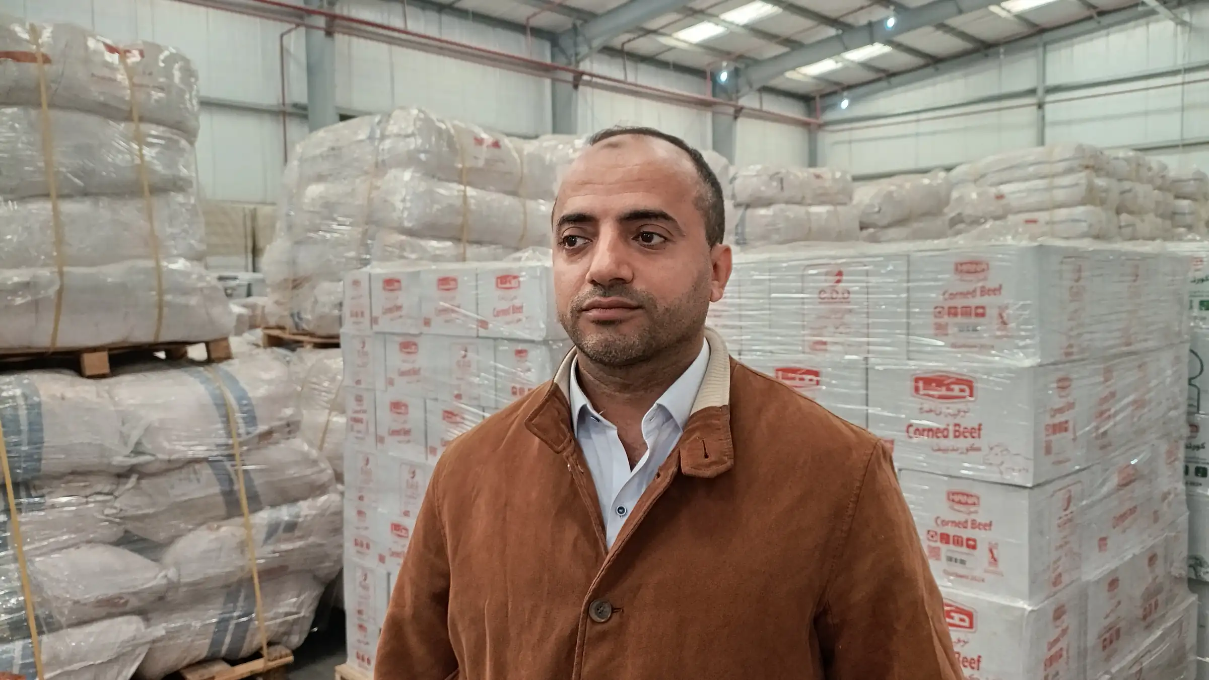 A team member in a supply warehouse stacked with palletised relief food and shelter goods