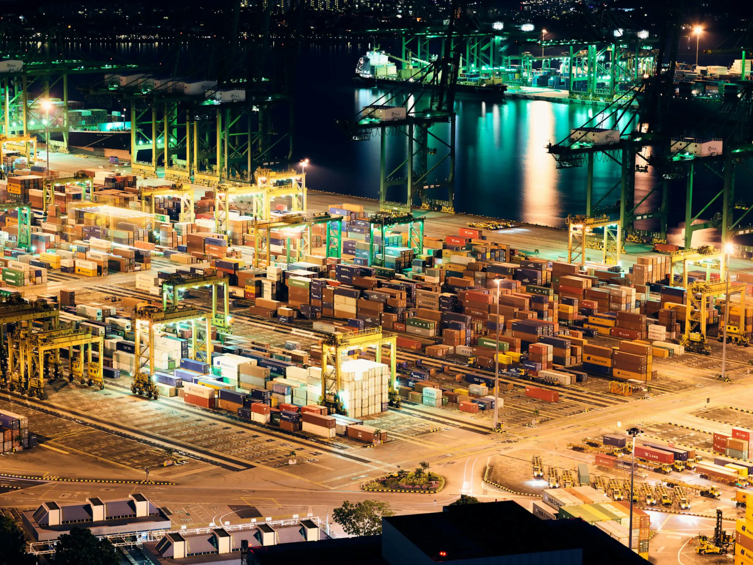 A container terminal at night, with cranes and stacked containers lit in warm light